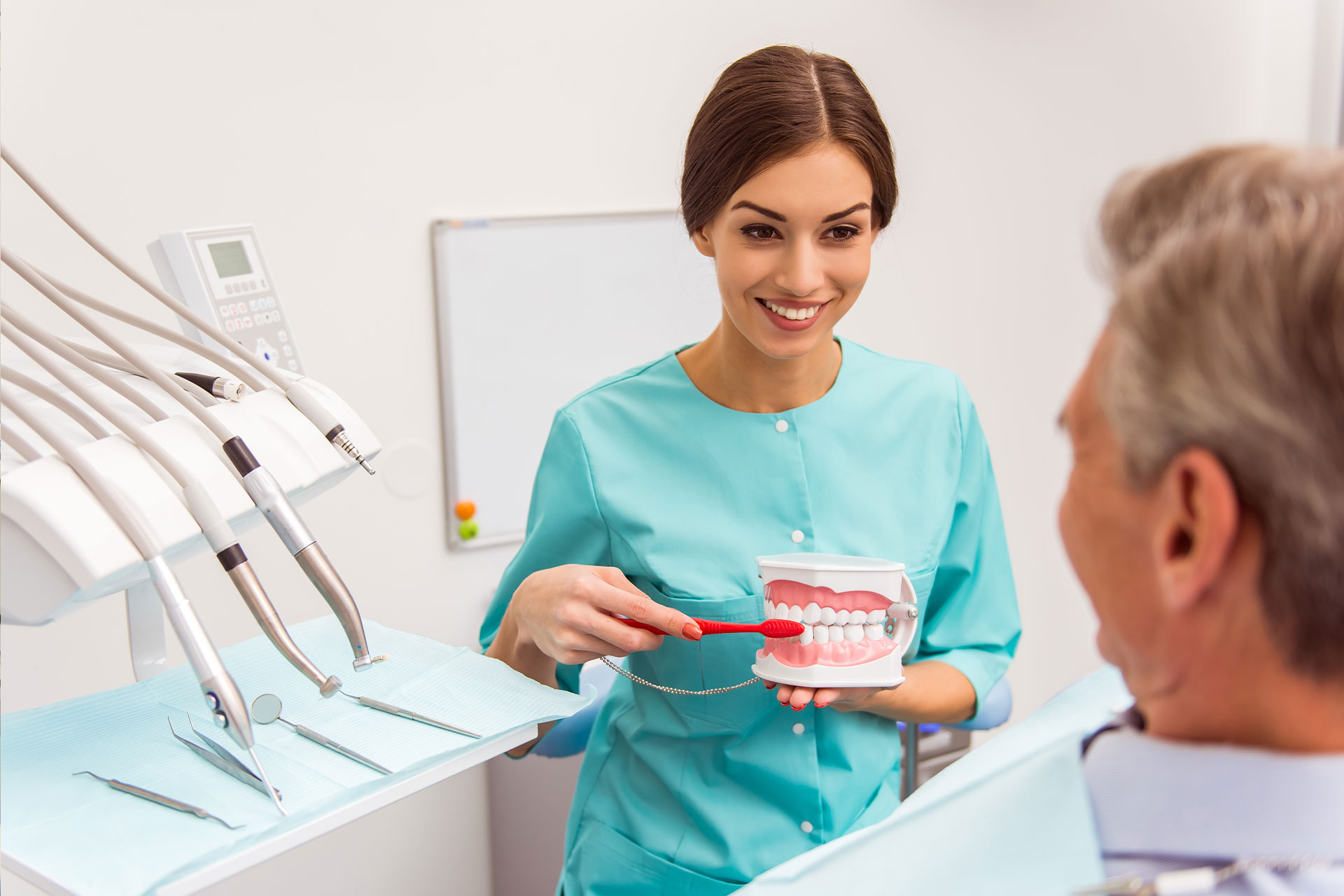 Higienista enseñando a un hombre canoso a cepillarse los dientes con un cepillo rojo y un modelo dental