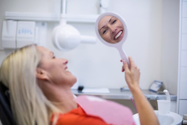 Paciente adulta revisándose la sonrisa en un espejo de mano en la consulta dental