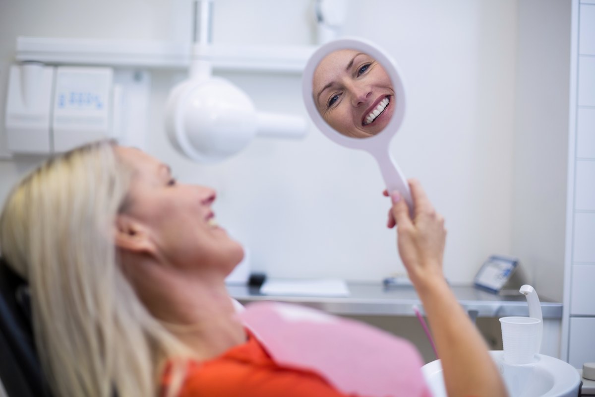 Paciente adulta revisándose la sonrisa en un espejo de mano en la consulta dental
