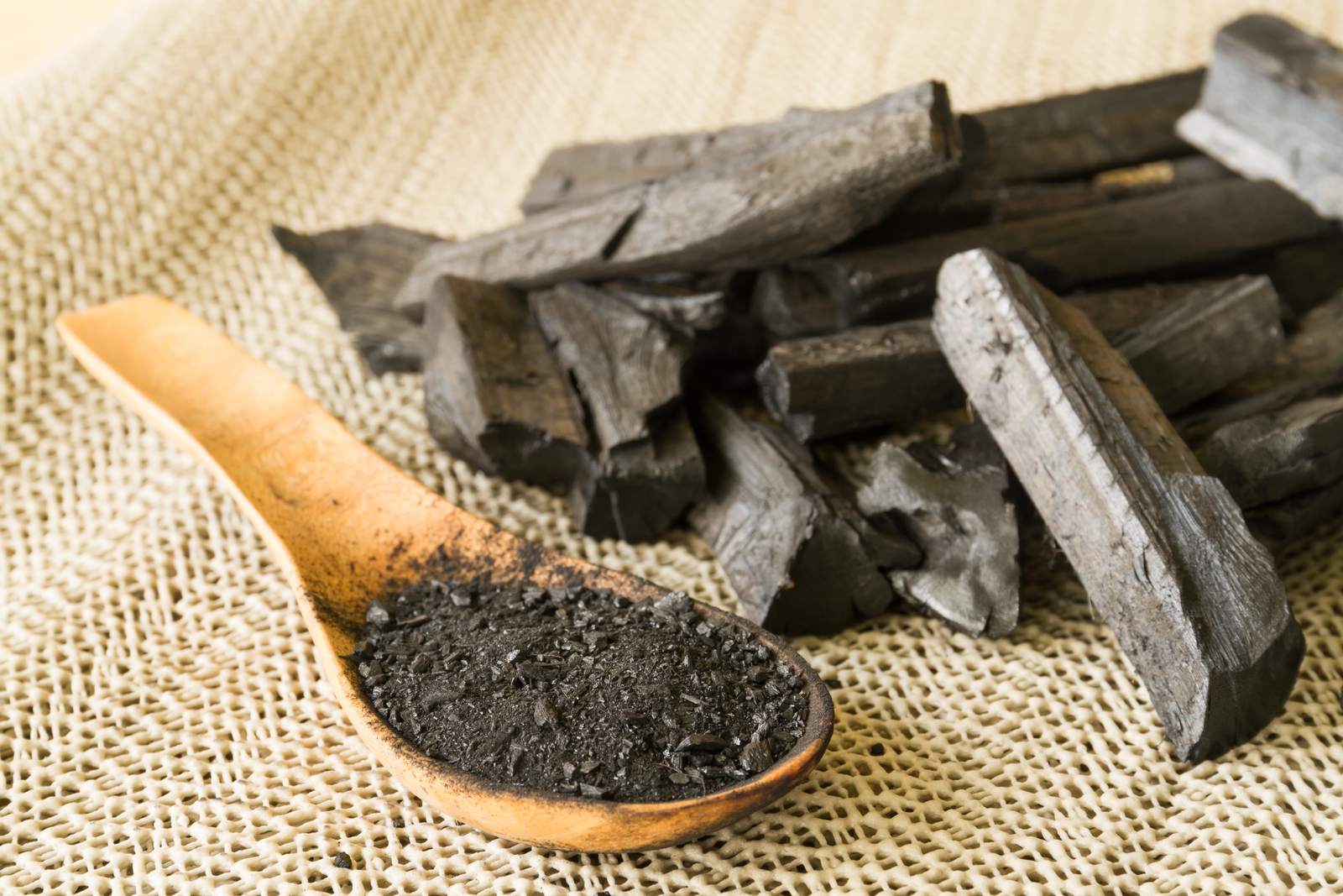 Cuchara de madera con carbón vegetal en polvo y trozos de carbón sobre una tela de yute