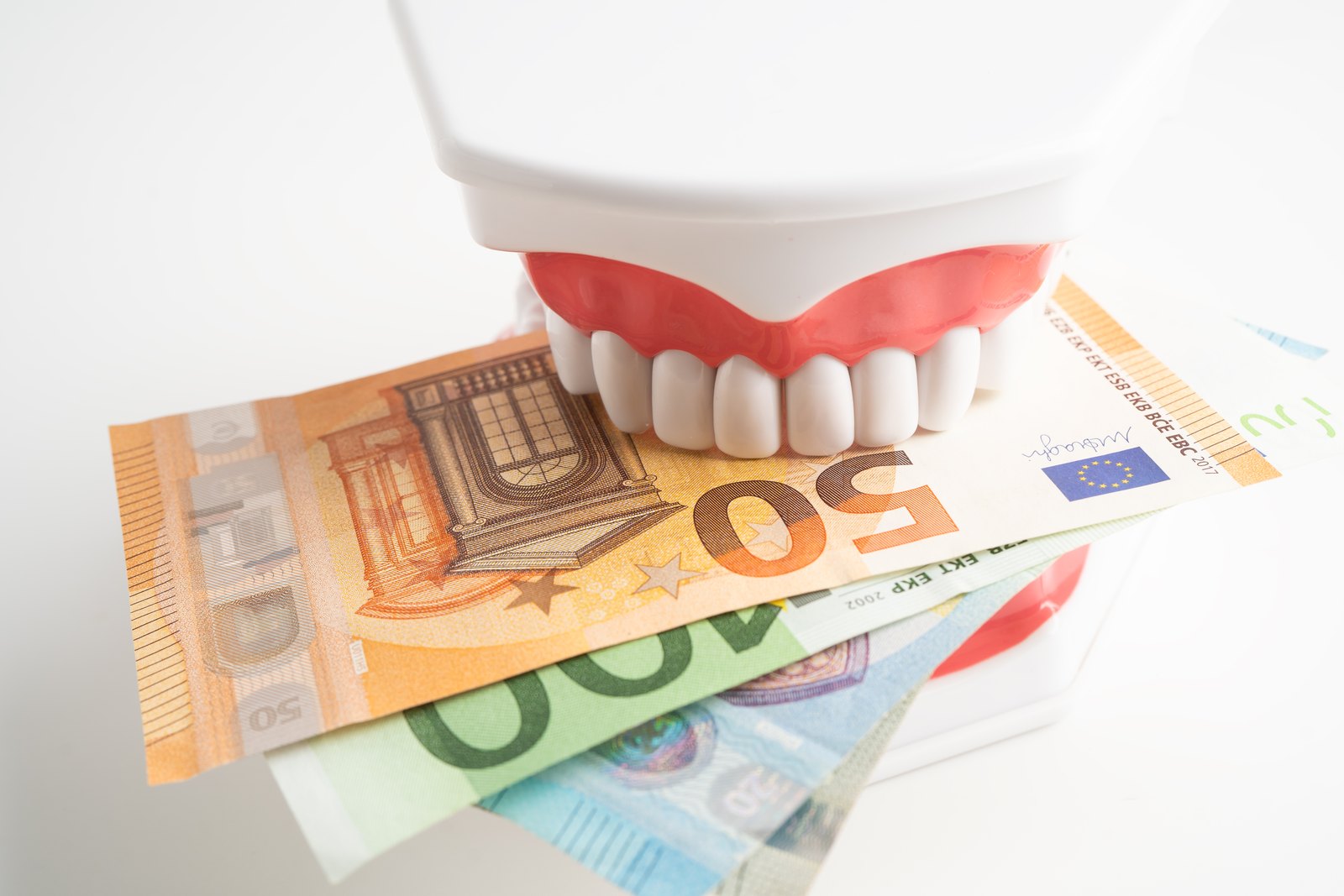 Modelo dental mordiendo varios billetes de euro sobre un fondo blanco