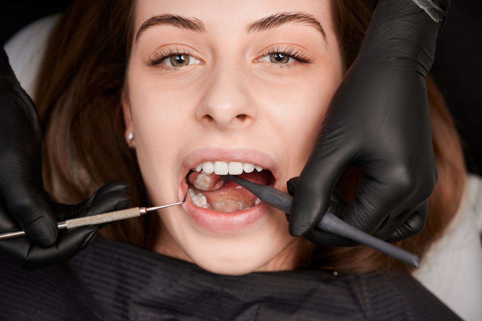 Dentista con guantes revisando los dientes de una paciente con un espejo y una sonda
