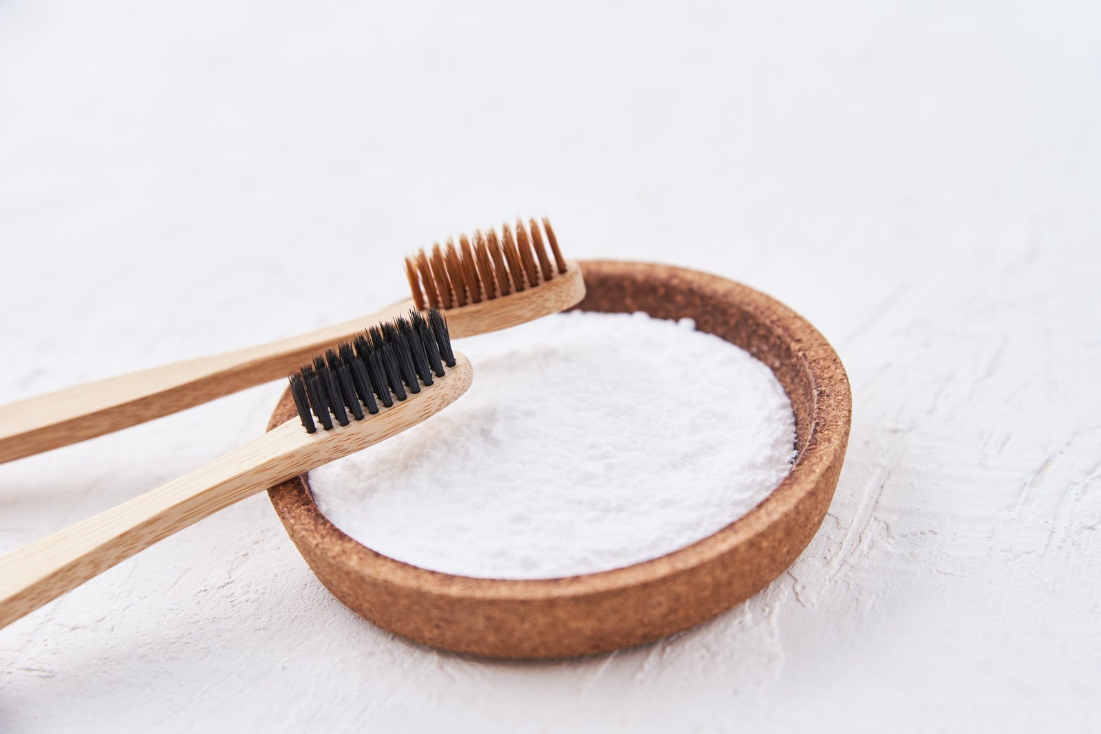 Cuenco de corcho con bicarbonato de sodio y dos cepillos de dientes de bambú