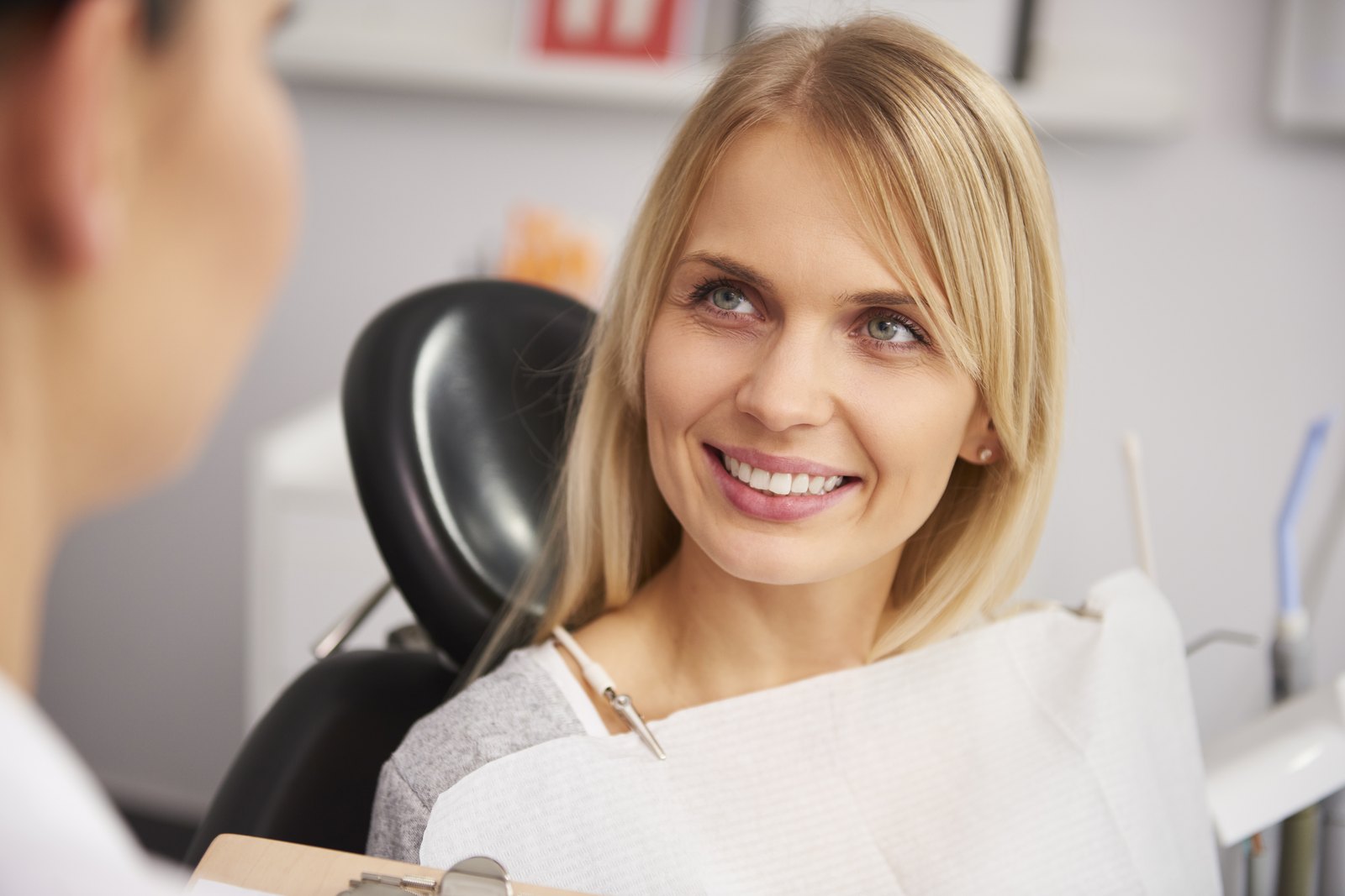 Paciente sonriendo en el sillón dental mientras habla con la dentista