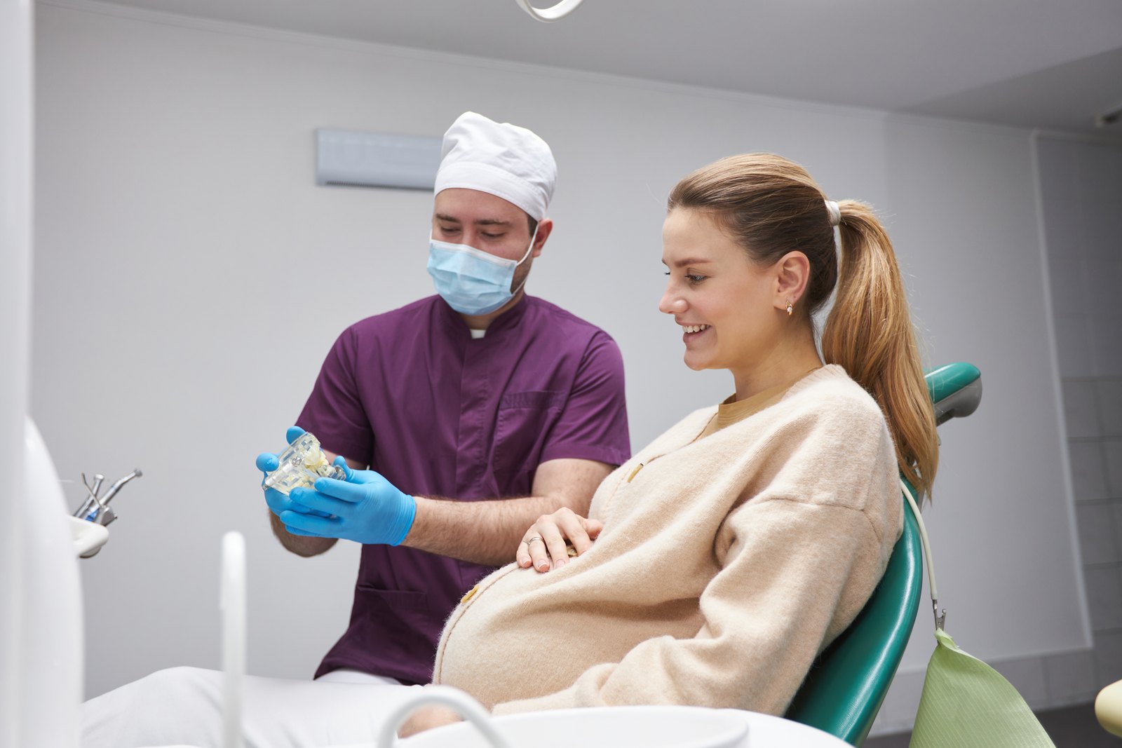 Mujer embarazada sonriendo en el sillón dental mientras el dentista le enseña un modelo dental