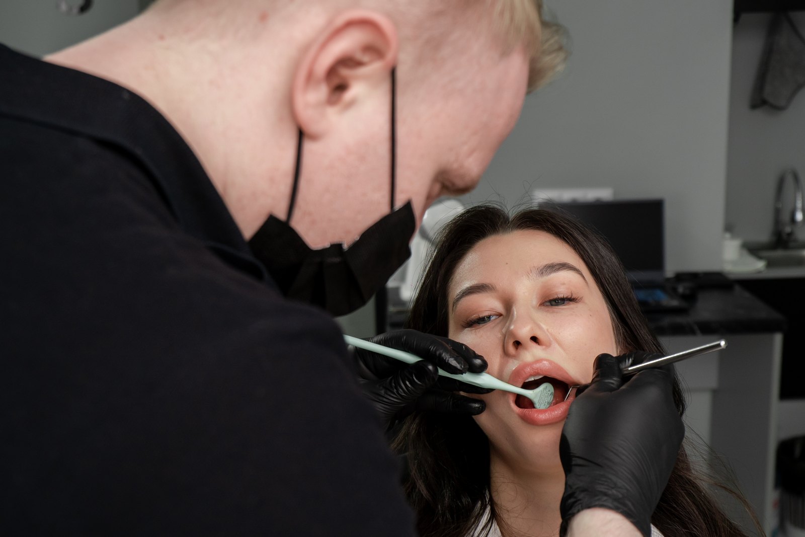 Dentista con guantes negros explorando la boca de una paciente con un espejo dental en la consulta